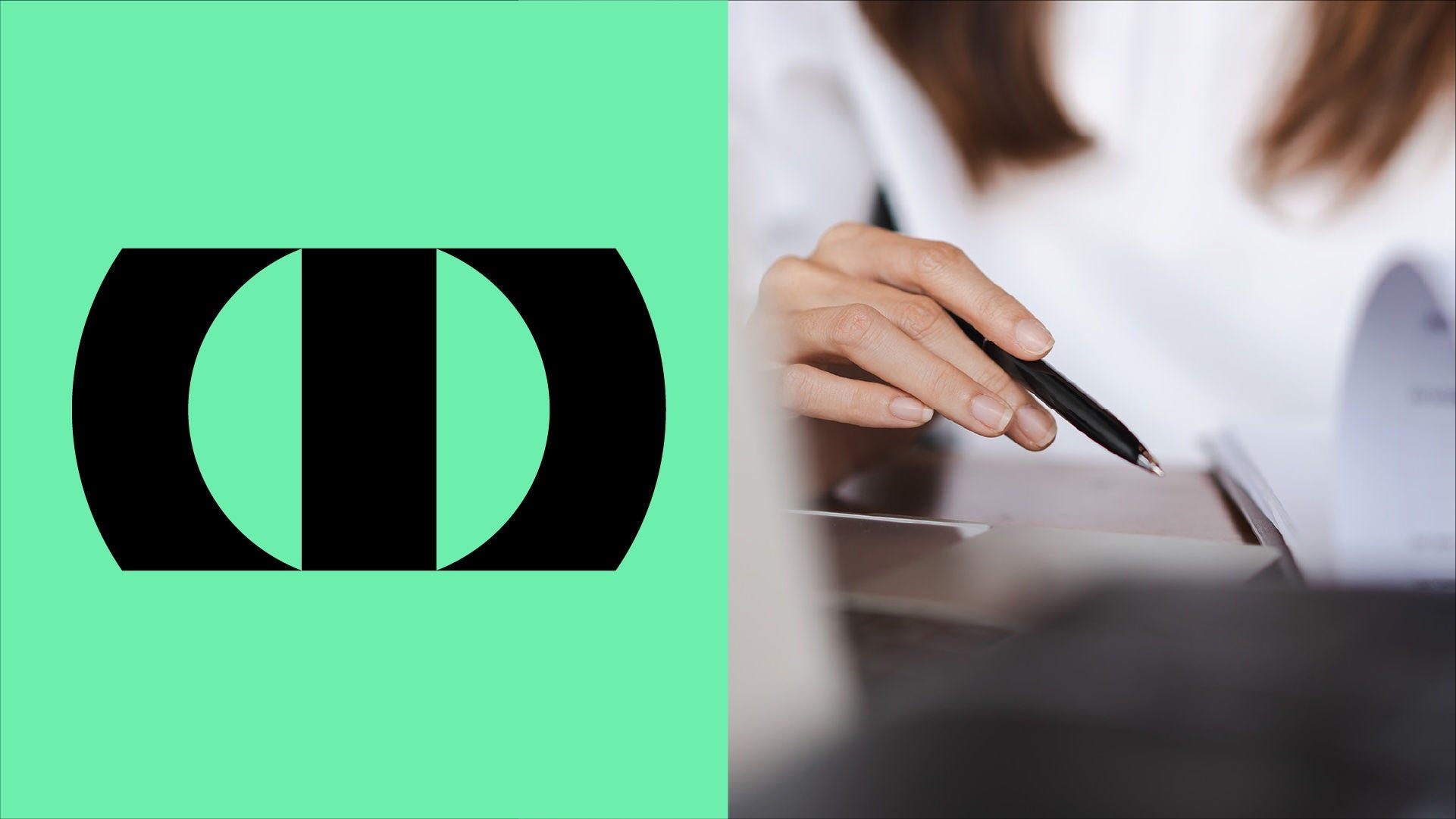 Close-up of a person’s hand holding a black pen and writing on paper at a desk, with an open document blurred in the background.