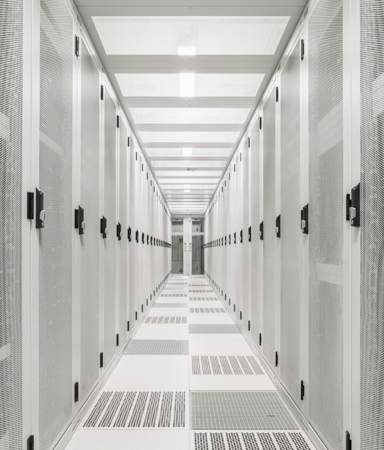 Aisle in a network server room where servers are locked behind grated doors